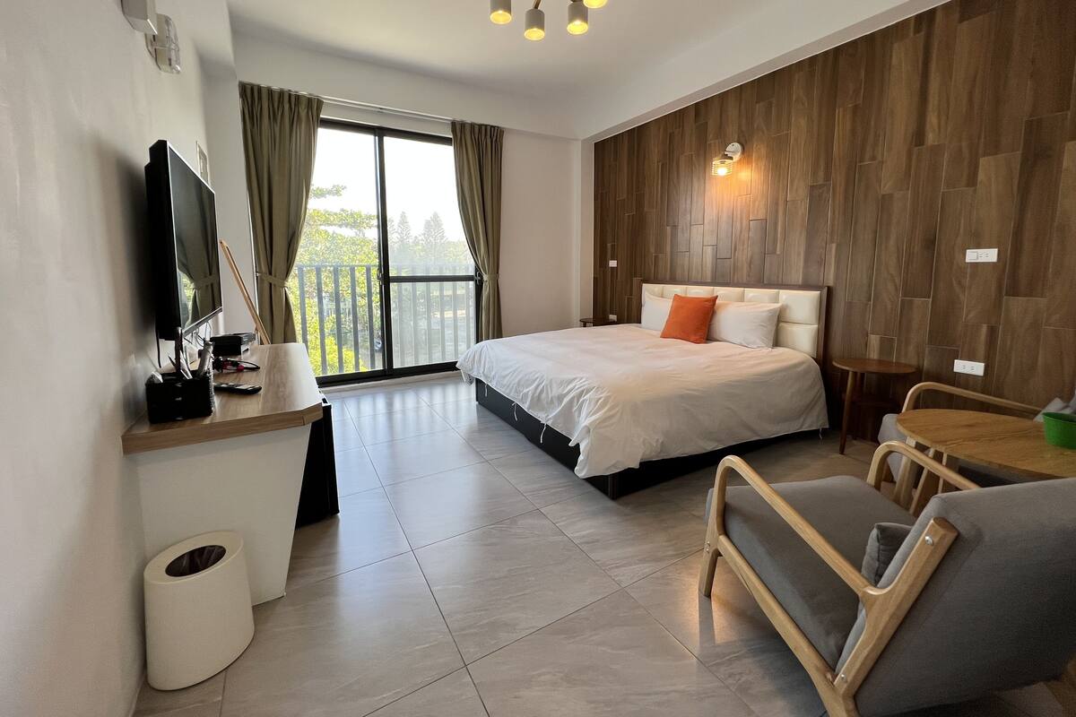 Habitació d'hotel moderna amb un llit gran, televisió, paret decorativa de fusta i un balcó amb cortines.