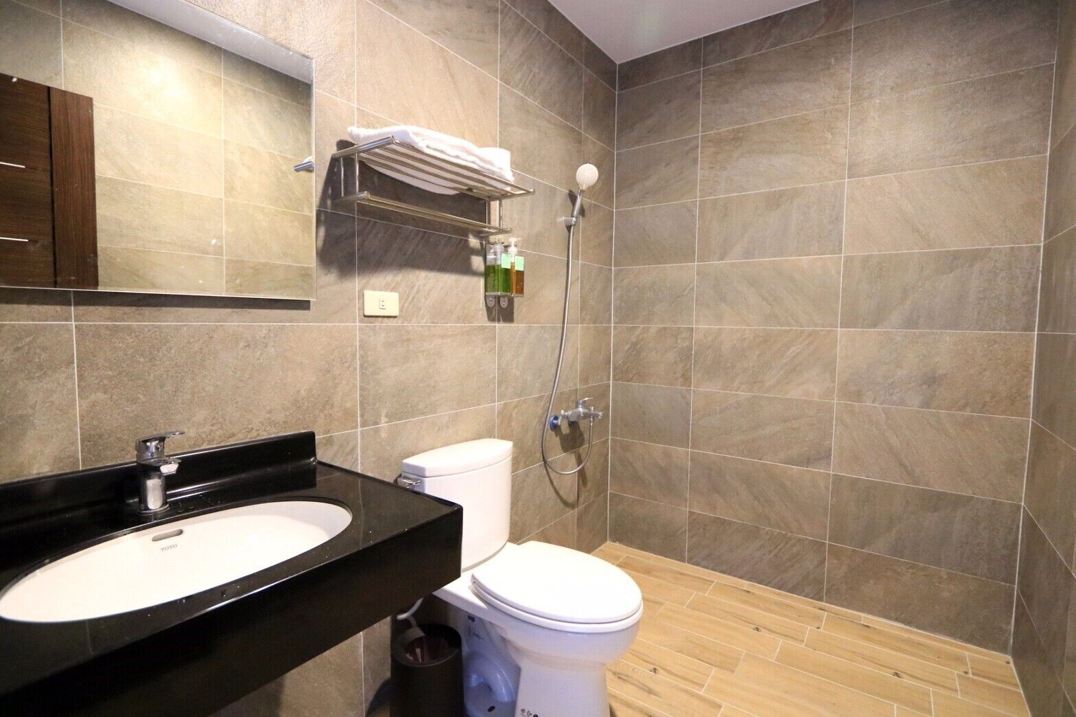 Une salle de bain moderne avec un lavabo noir, des toilettes blanches et une douche équipée d’un pommeau de douche à main.