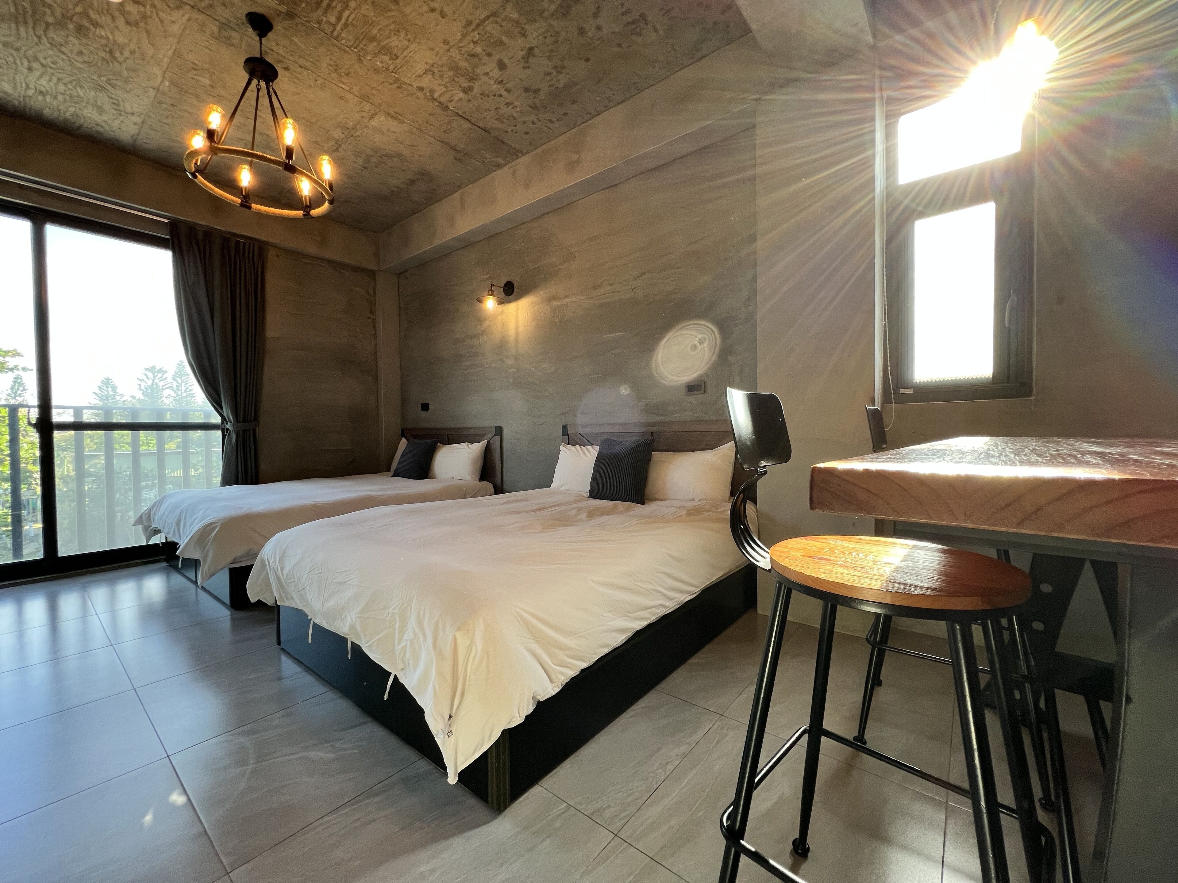 A modern bedroom with two beds, a wooden table, and a large window.
