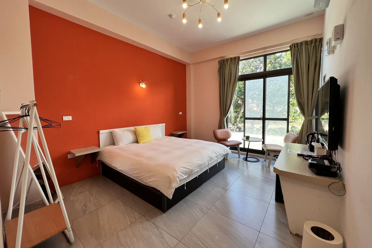 Habitació d'hotel amb llit, escriptori amb ordinador, cadira, taula petita i finestra amb cortines.