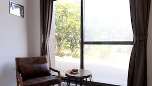 Una habitación con un ventanal grande, una silla y una mesita con un florero.