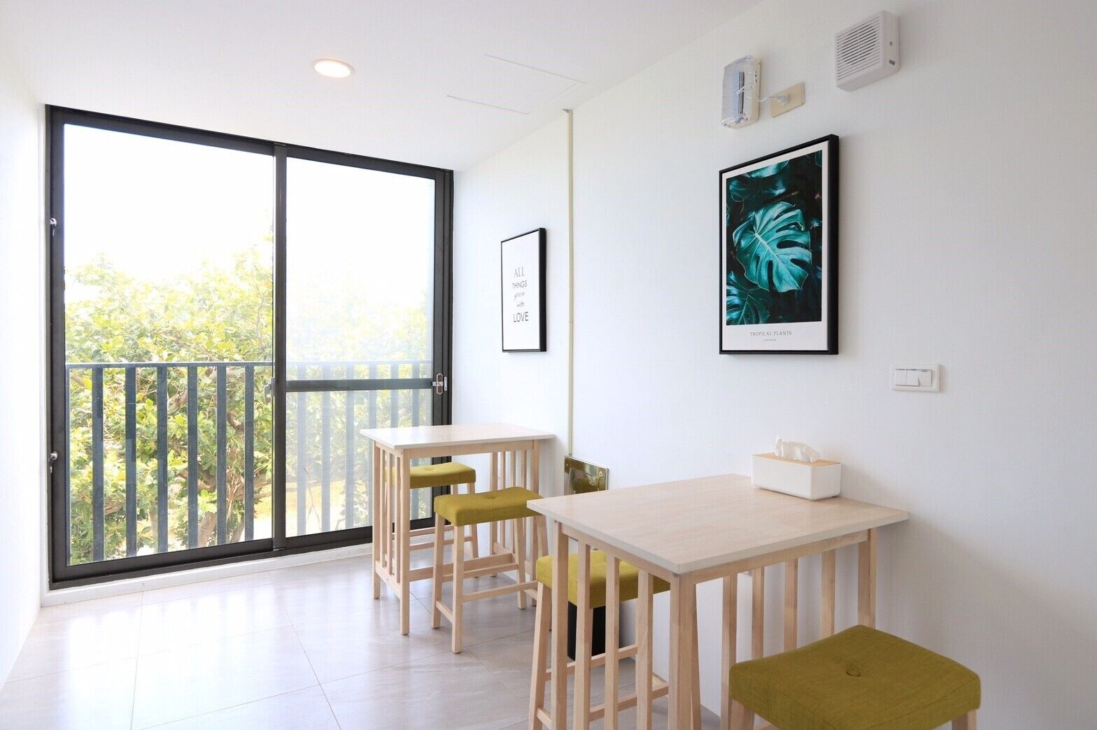 A room with a large sliding glass door leading to a balcony, a small wooden table with two chairs, and a framed picture on the wall.