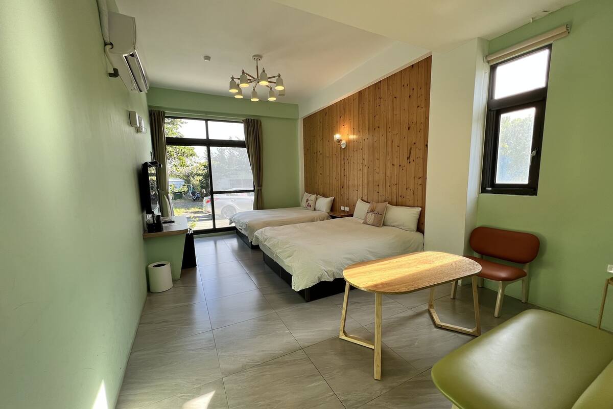 Habitació d'hotel moderna amb dos llits, una paret d'accent de fusta, una finestra gran i una cadira verda.
