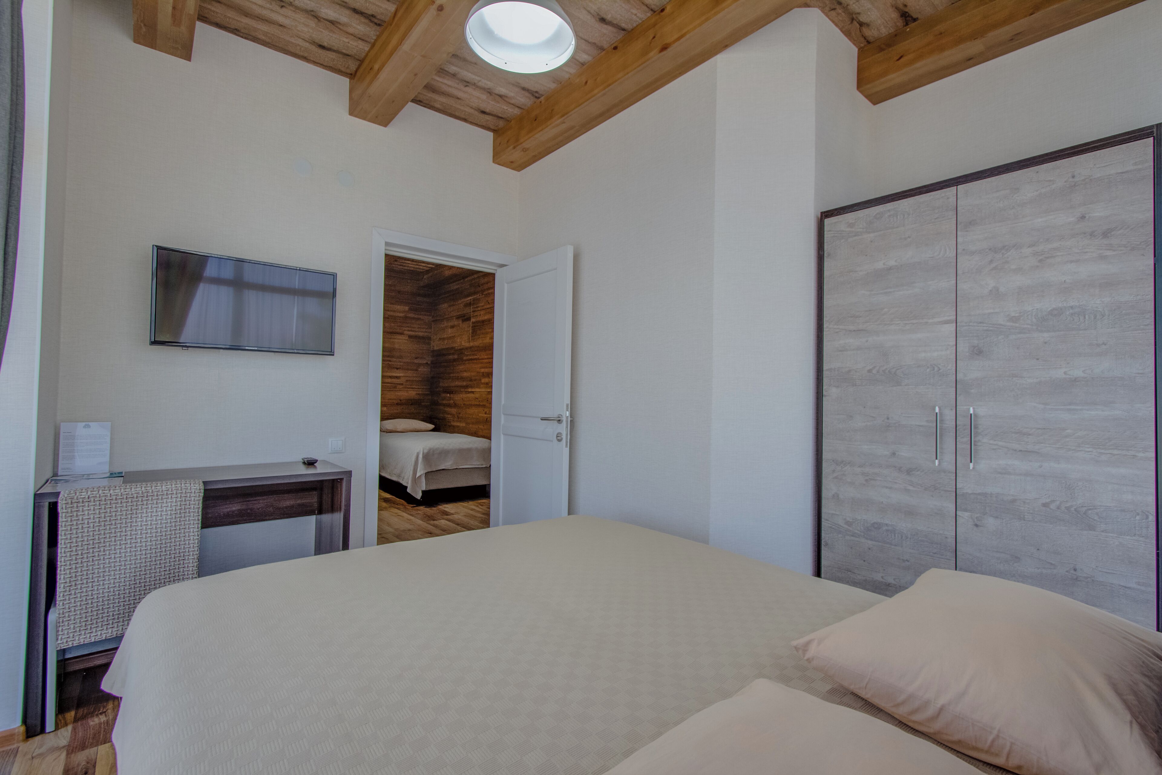 A bedroom with a large bed, a wardrobe, a desk, and a television.