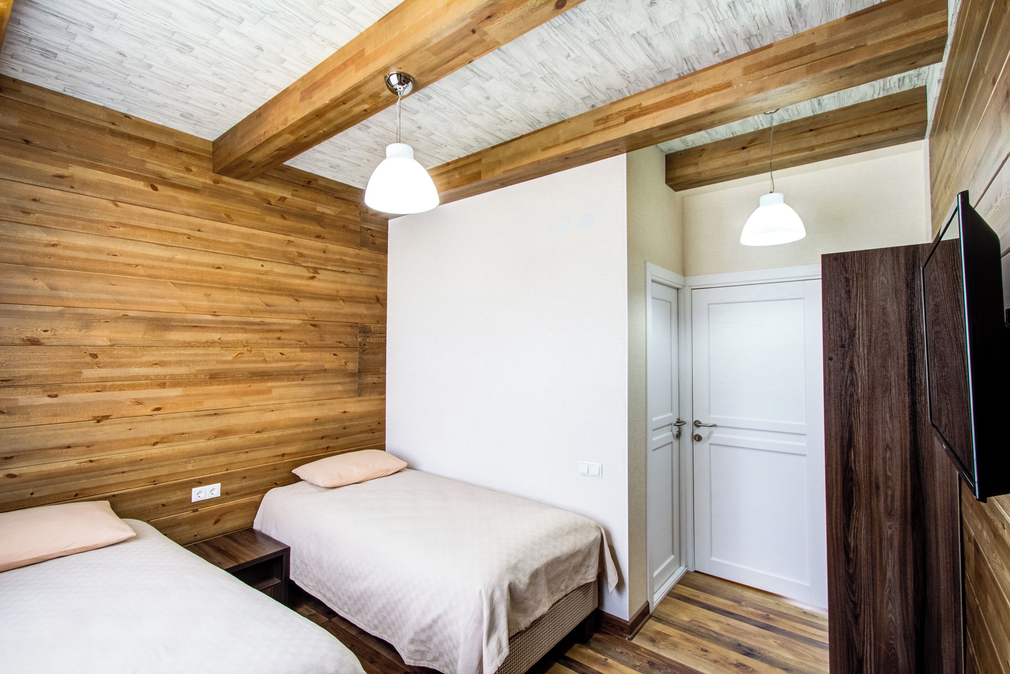Een kamer met houten wanden en plafond, twee bedden met witte beddengoed, een witte deur en een tv aan de muur.