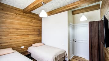 Una stanza con pareti e soffitto in legno, due letti con biancheria bianca, una porta bianca e un televisore a parete.