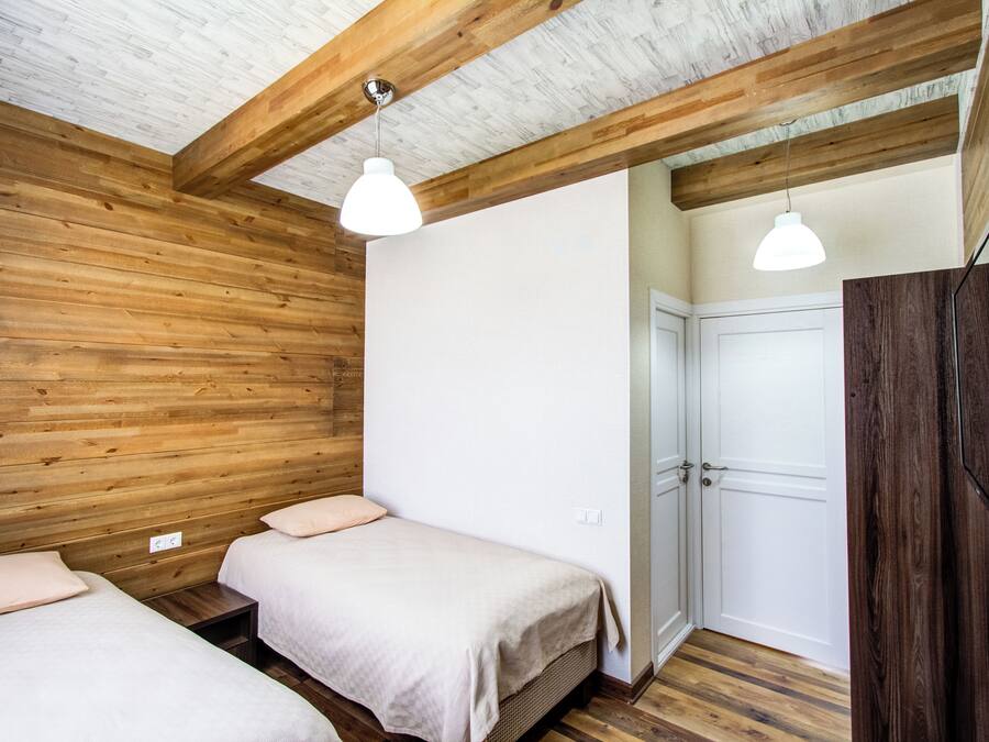Una stanza con pareti e soffitto in legno, due letti con biancheria bianca, una porta bianca e un televisore a parete.