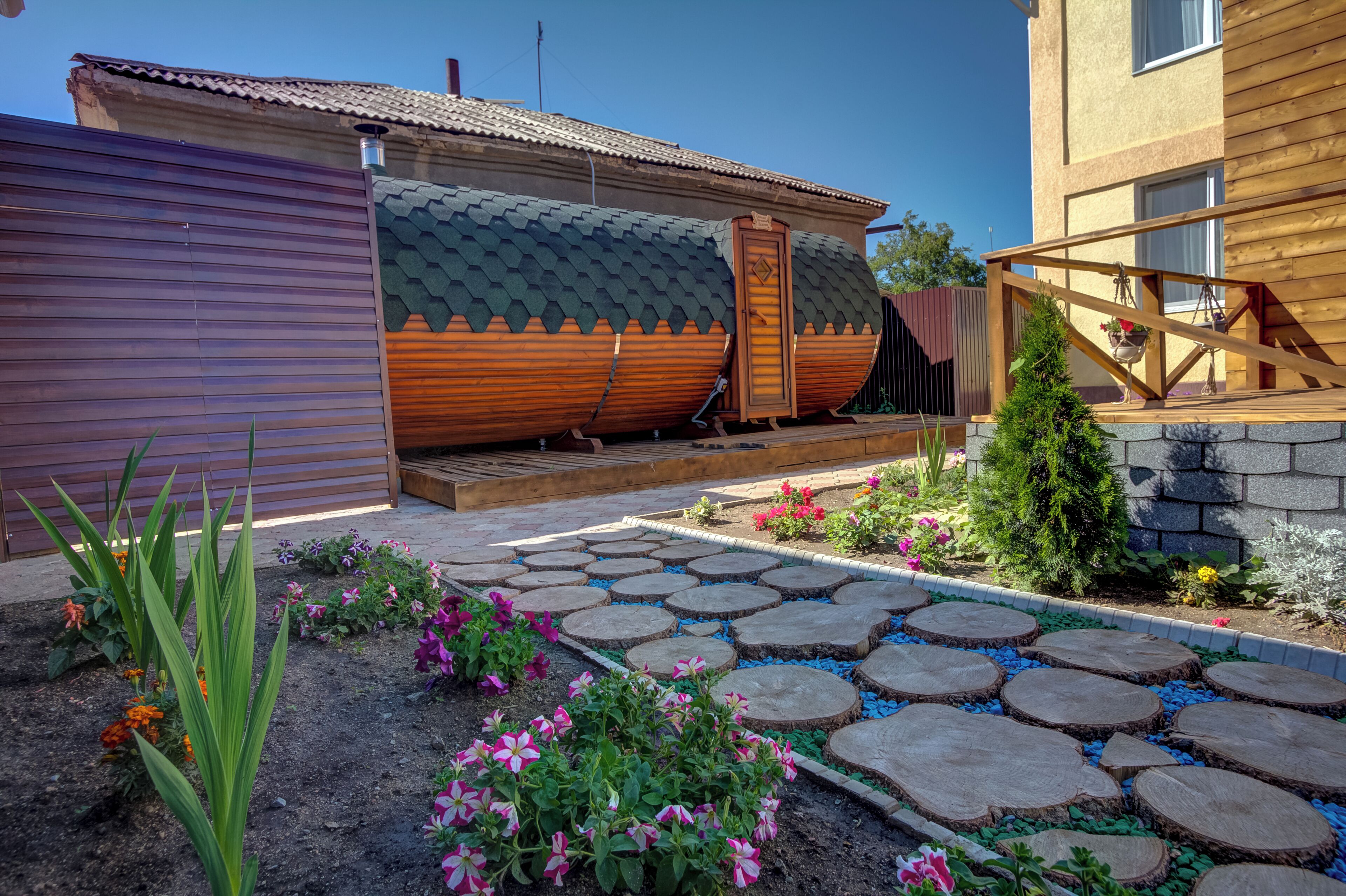 A garden with a stone pathway, wooden deck, and various plants.