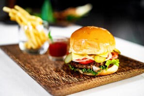 Hamburguesa con lechuga, tomate y queso, servida sobre una tabla de madera con papas fritas y kétchup al fondo.