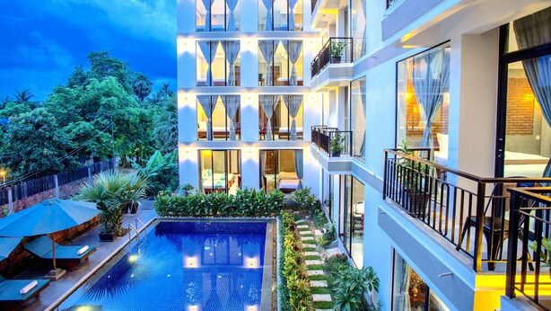 Un hôtel à plusieurs étages doté d’une piscine sur le toit, de balcons et d’une végétation luxuriante.