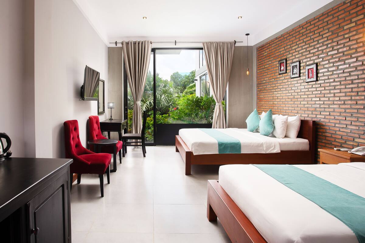 A modern hotel room with a large bed, a desk with a chair, and a view of greenery through the window.