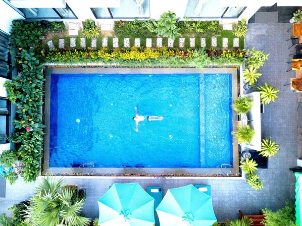 Una piscina en la azotea con una persona nadando, rodeada de exuberante vegetación y mobiliario de exterior.