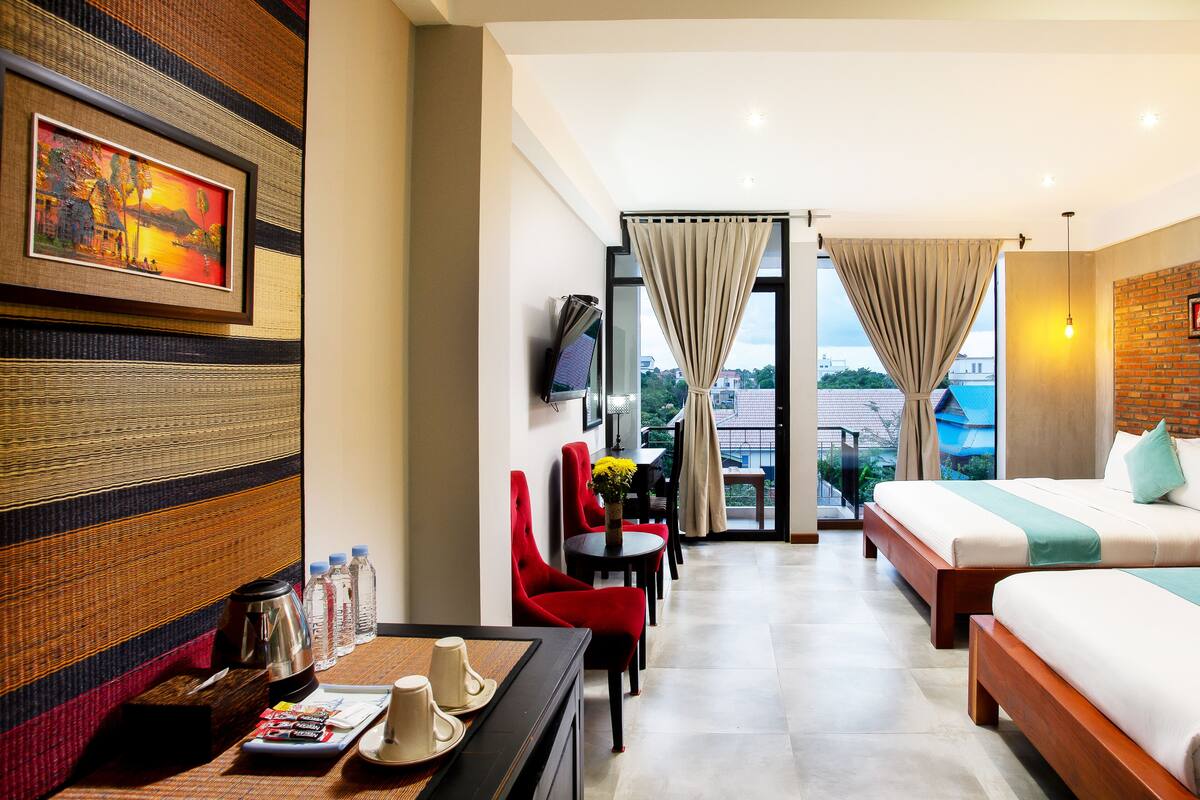 A hotel room with a bed, a desk with a coffee pot, a TV, and a view of the outside.