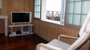 A wooden-paneled room with a television, a fan, and a window with a view of a rocky landscape. - Sunny Namwon (Seogwipo)