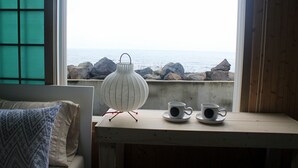 A room with a view of the sea, a wooden table with two cups and saucers, and a white lamp. - Sunny Namwon (Seogwipo)