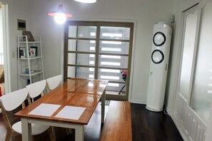 Ein Essbereich mit einem Holztisch, weißen Stühlen, einem weißen Bücherregal und einem großen Fenster mit Jalousien.