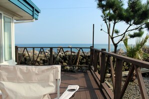 Eine Holzterrasse mit einem weißen Stuhl und einem kleinen Tisch, mit Blick auf eine felsige Küstenlinie und das Meer.