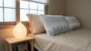 A bedroom with a bed, pillows, a bedside lamp, and a window. - Sunny Namwon (Seogwipo)