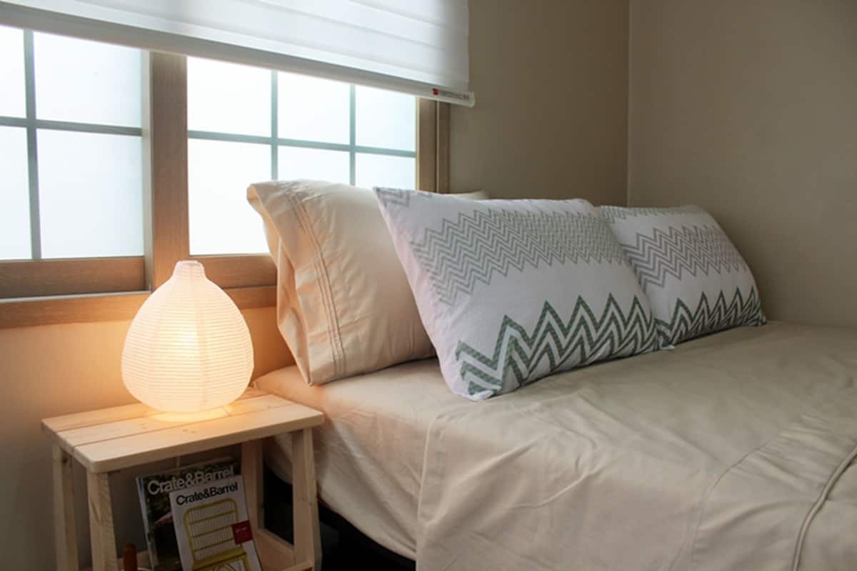 A bedroom with a bed, pillows, a bedside lamp, and a window.