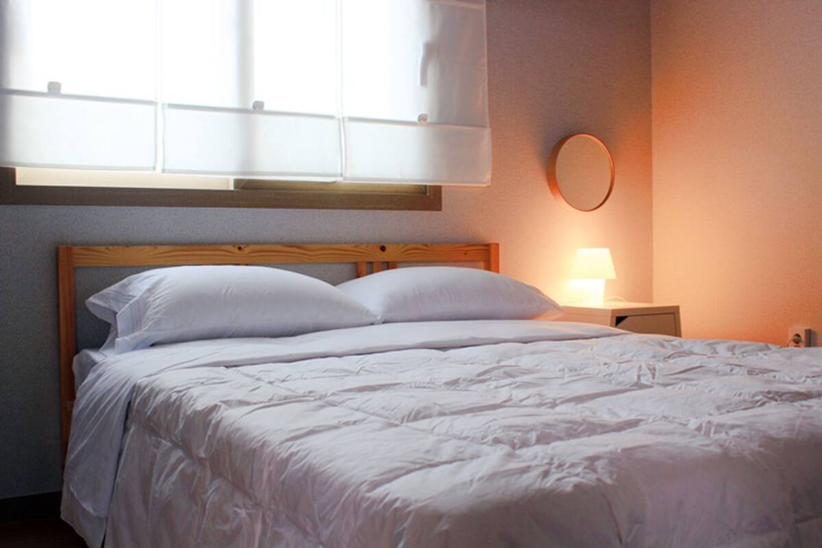Un lit bien fait, avec une literie blanche et une tête de lit en bois, une lampe de chevet et un miroir rond accroché au mur.