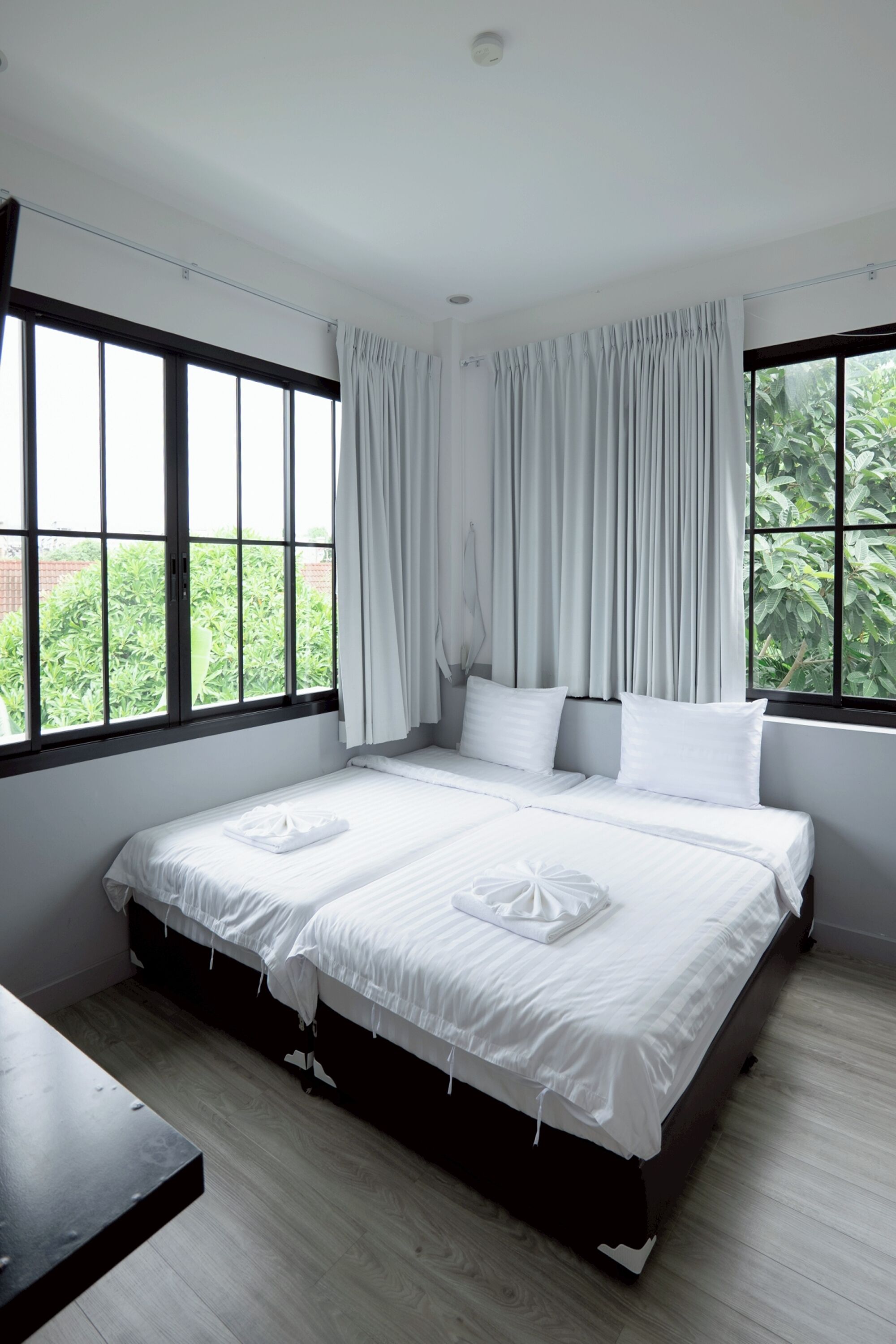 A bedroom with a large bed, two pillows, white curtains, and a view of greenery outside.
