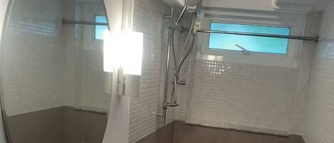A modern bathroom with a white sink, a large mirror, and a shower area.