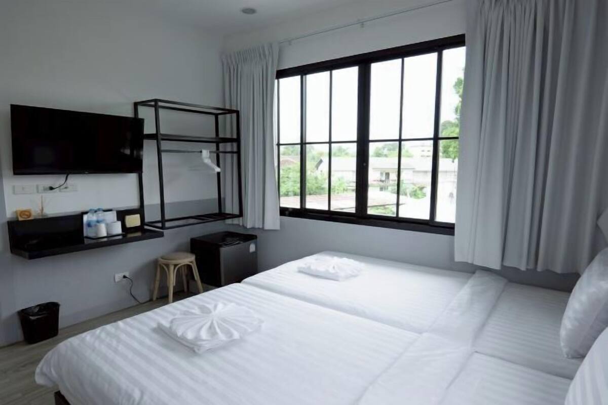 Ein Hotelzimmer mit großem Fenster, einem an der Wand montierten Fernseher, einem Etagenbett, einem kleinen Hocker und einem Mülleimer.