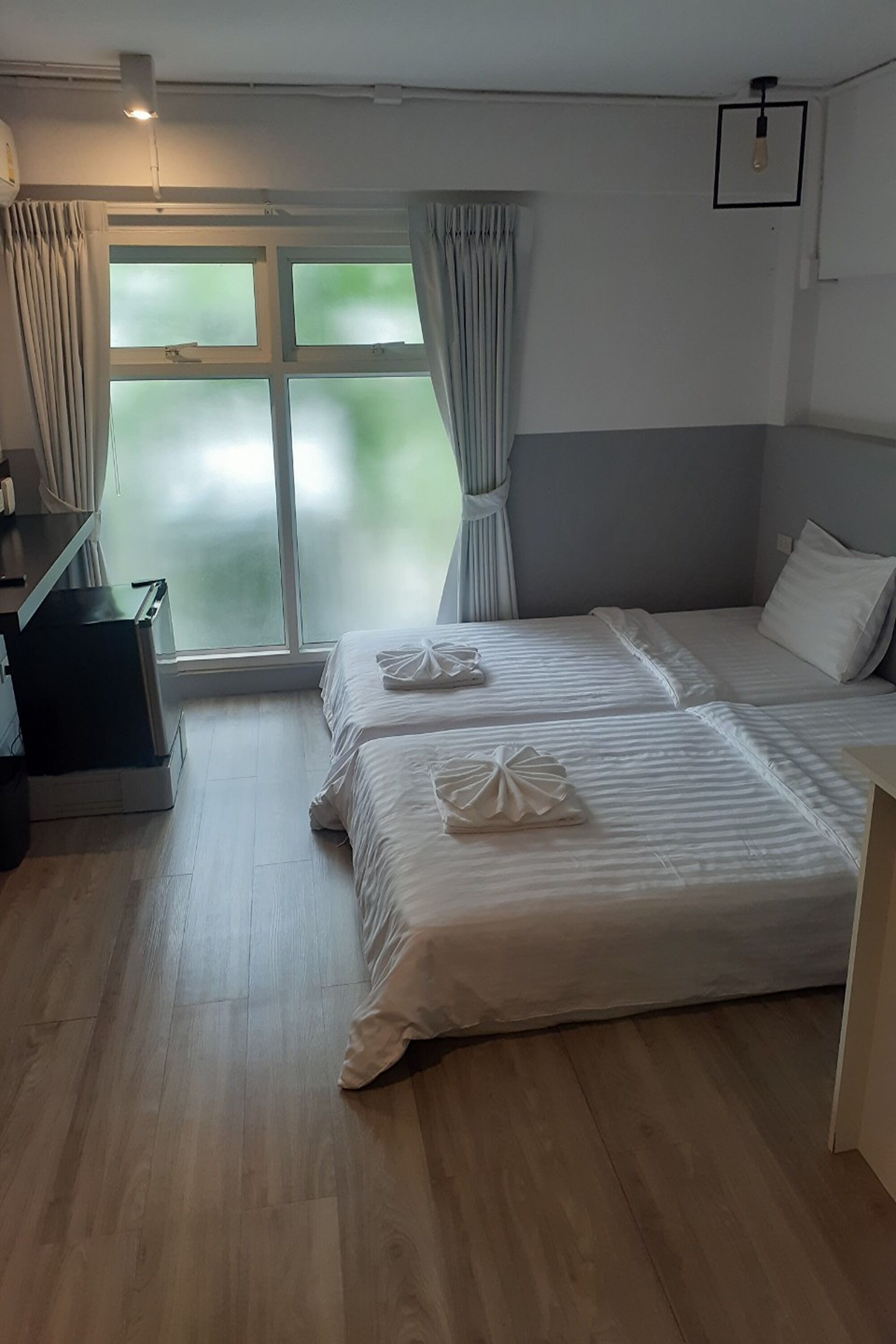 A hotel room with two beds, a desk, and a large window with curtains.