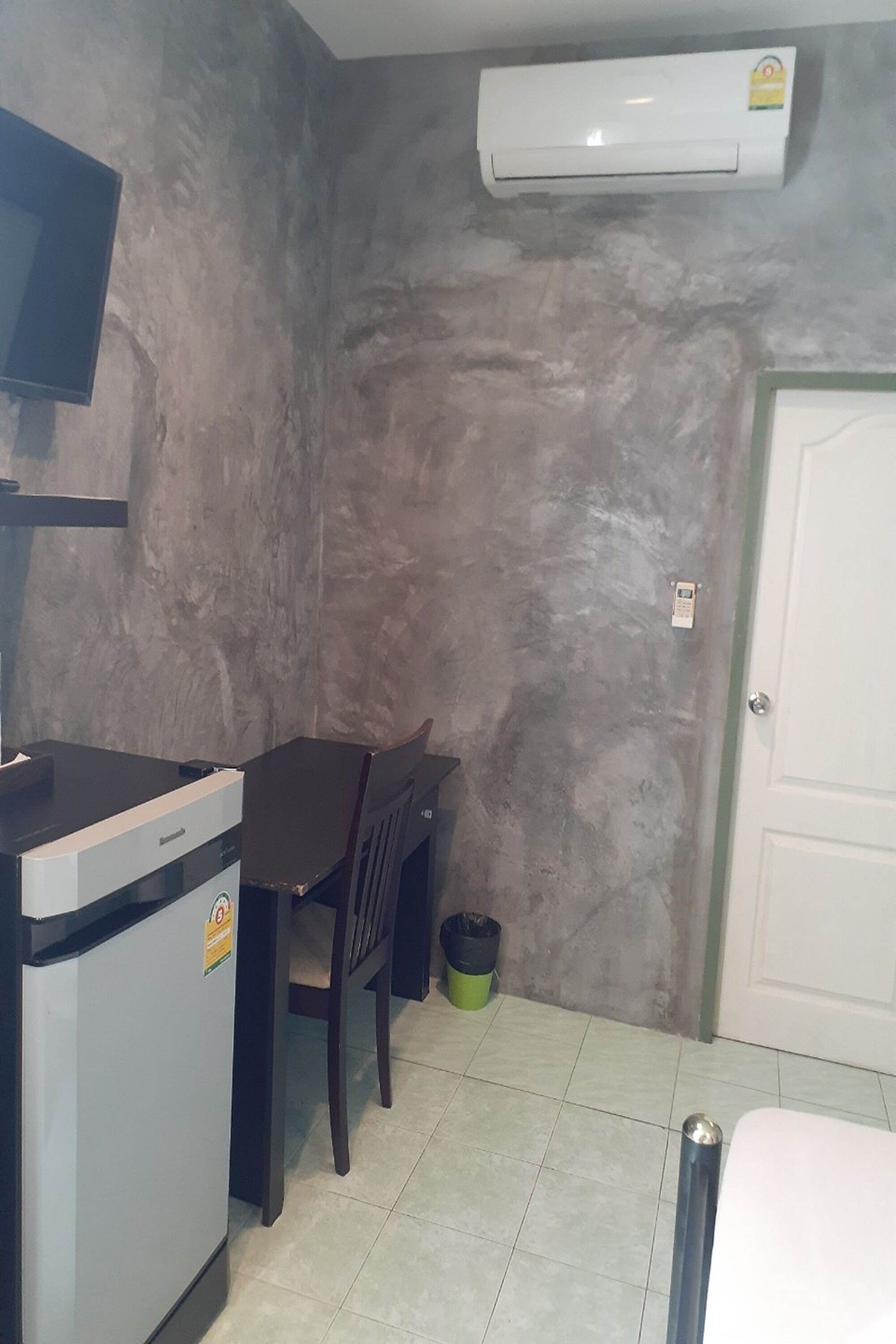Habitación compacta con kitchenette, una sola silla, un cesto de basura pequeño y una puerta blanca.