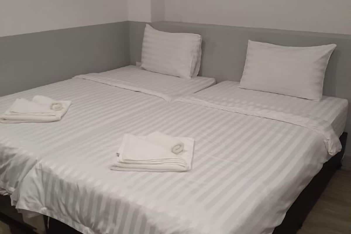 Ein ordentlich bezogenes Doppelbett mit weißer Bettwäsche und Kissen, ein gefaltetes Handtuch auf dem Bett, und eine graue Wand im Hintergrund.
