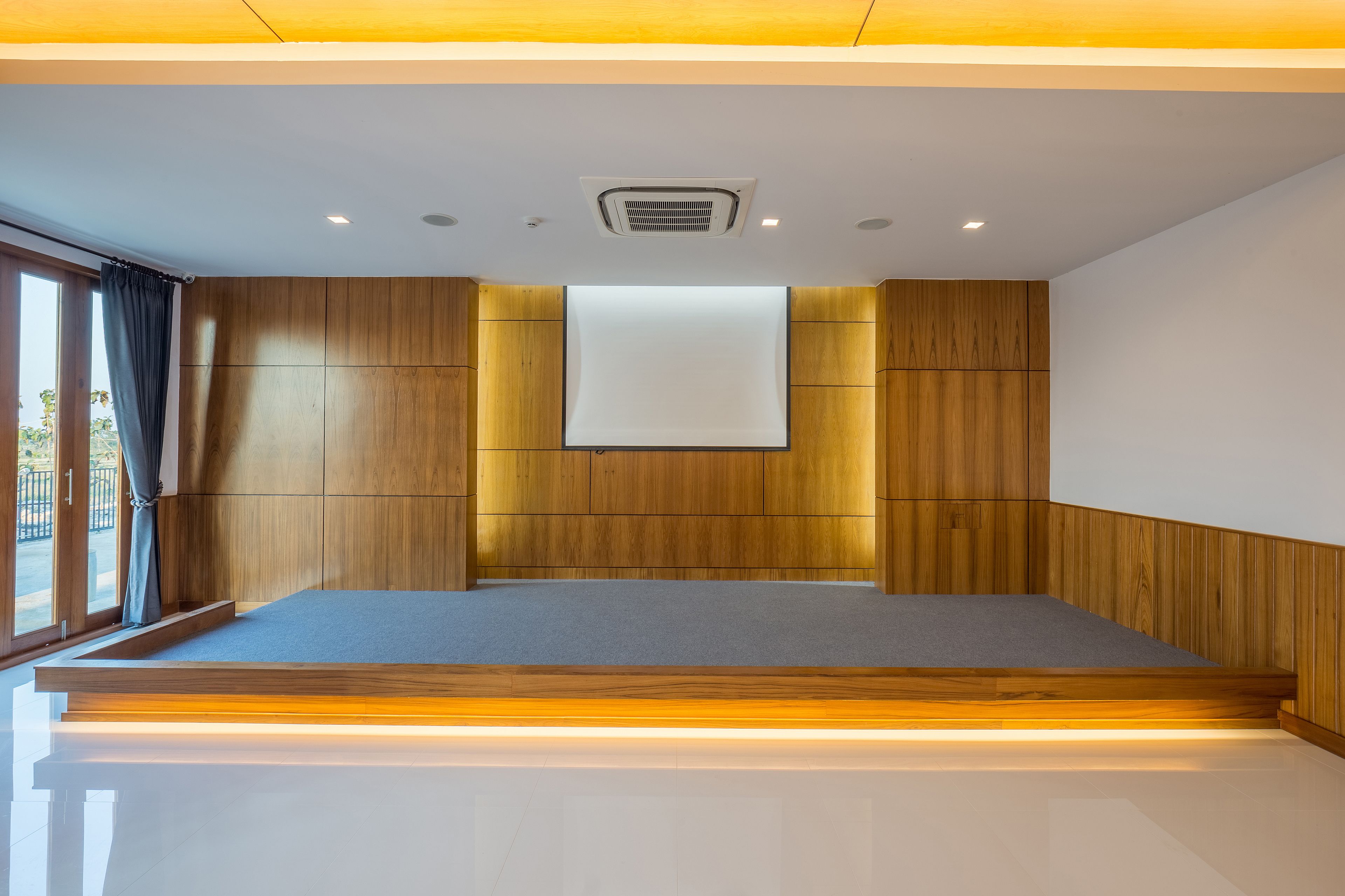 Una habitación moderna con un panel de madera en la pared, un ventanal con cortinas, un televisor de pantalla plana montado y una plataforma de madera al pie de la cama.