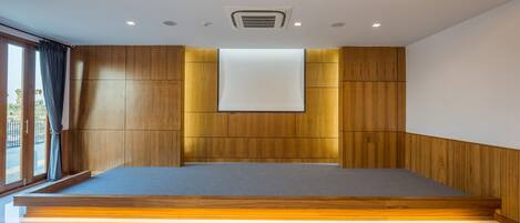 Una habitación moderna con un panel de madera en la pared, un ventanal con cortinas, un televisor de pantalla plana montado y una plataforma de madera al pie de la cama.