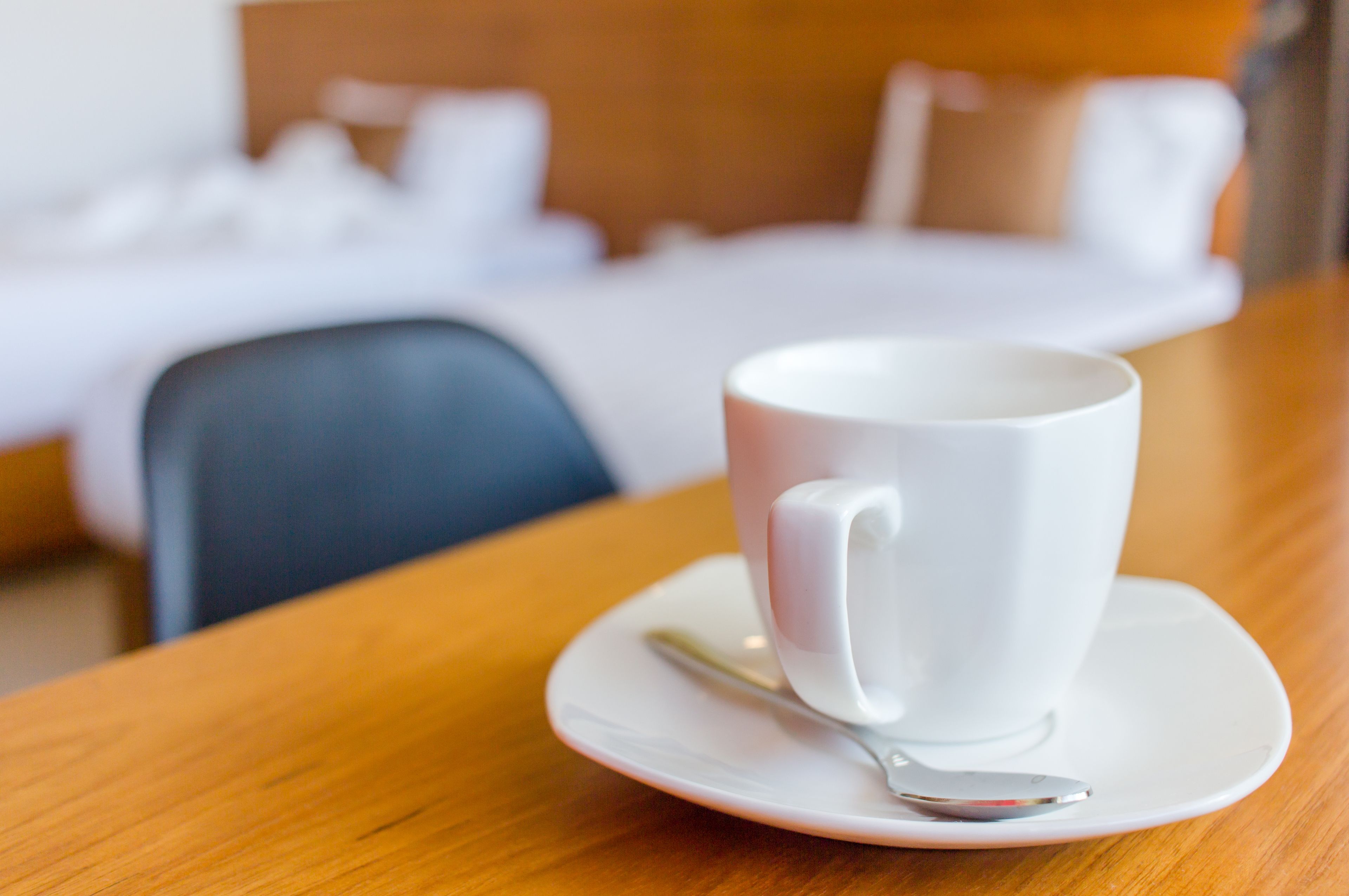 Una taza blanca sobre un platito con una cuchara en una mesa de madera en una habitación de hotel.
