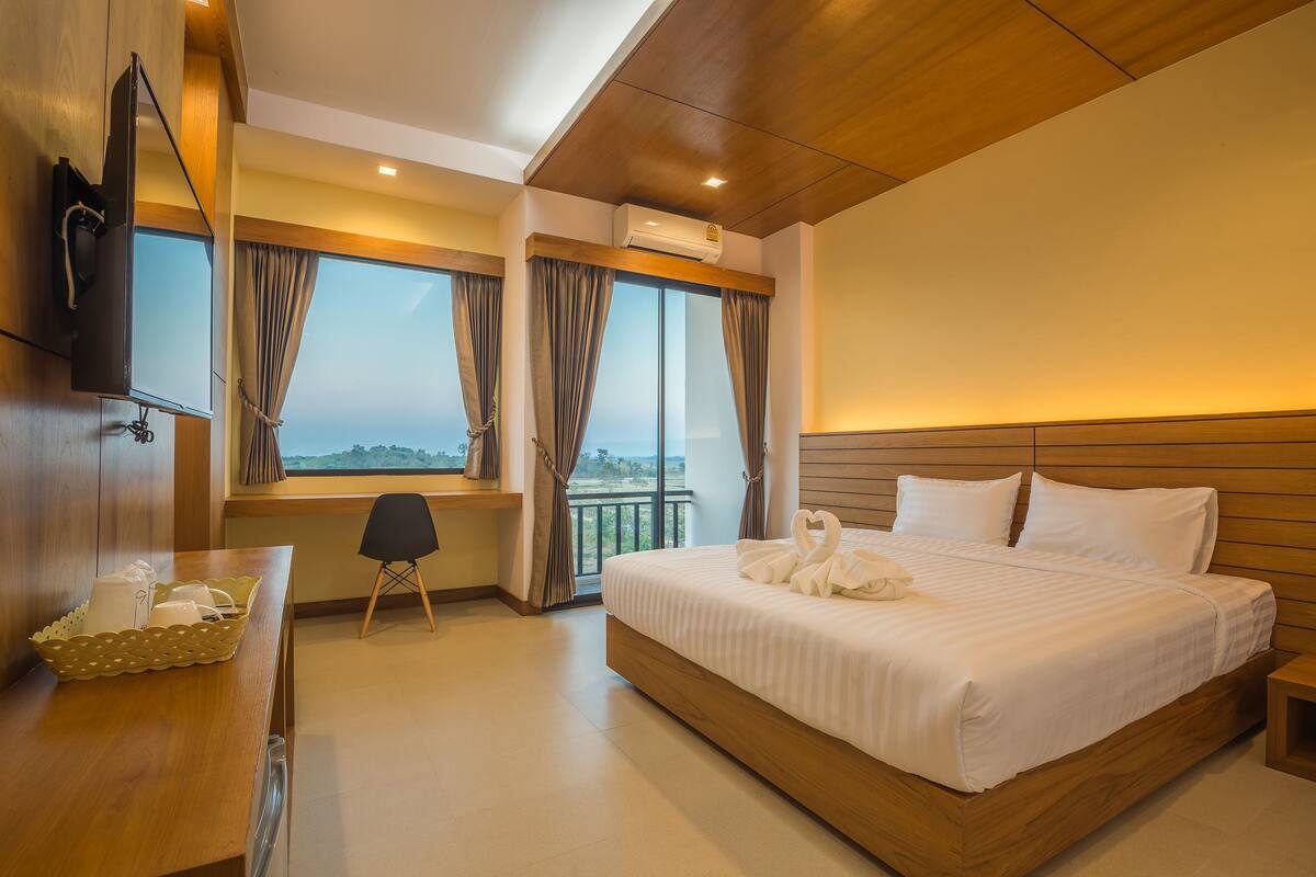 A hotel room with a large bed, a desk with a basket, a chair, and a TV mounted on the wall.