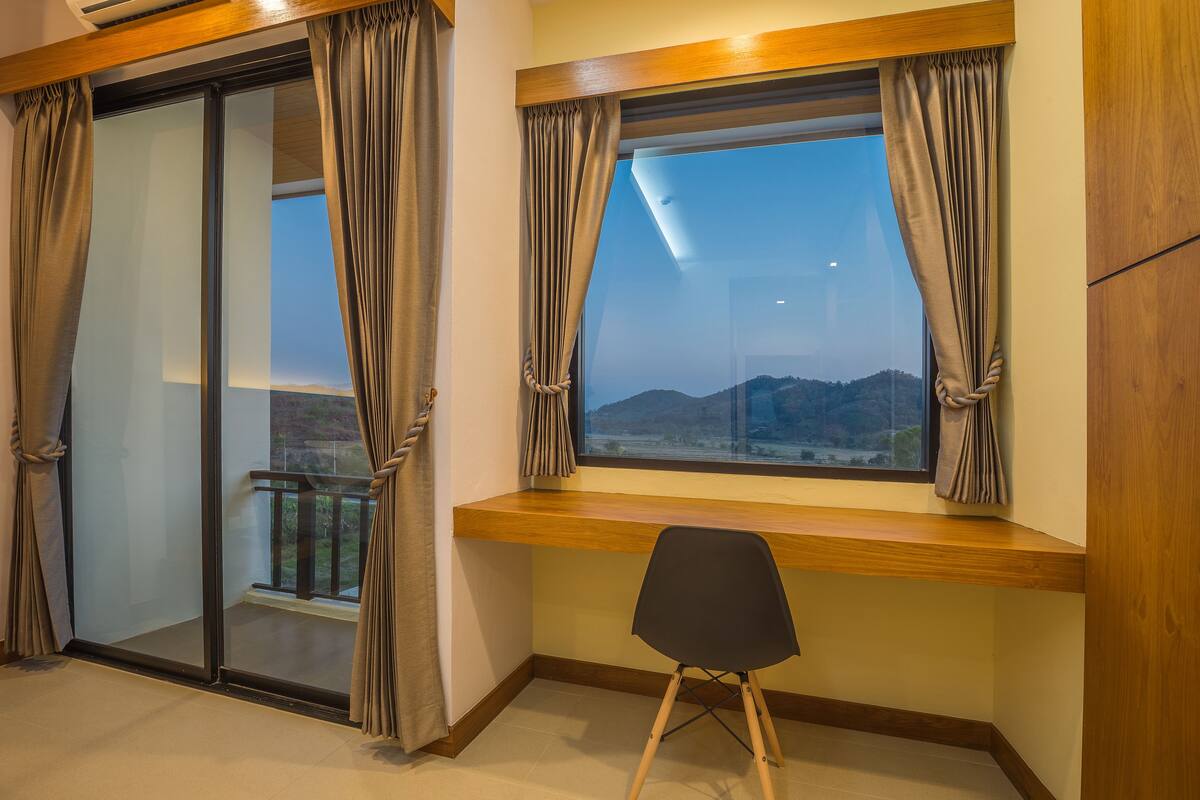 A room with a large window, a wooden desk, and a chair.