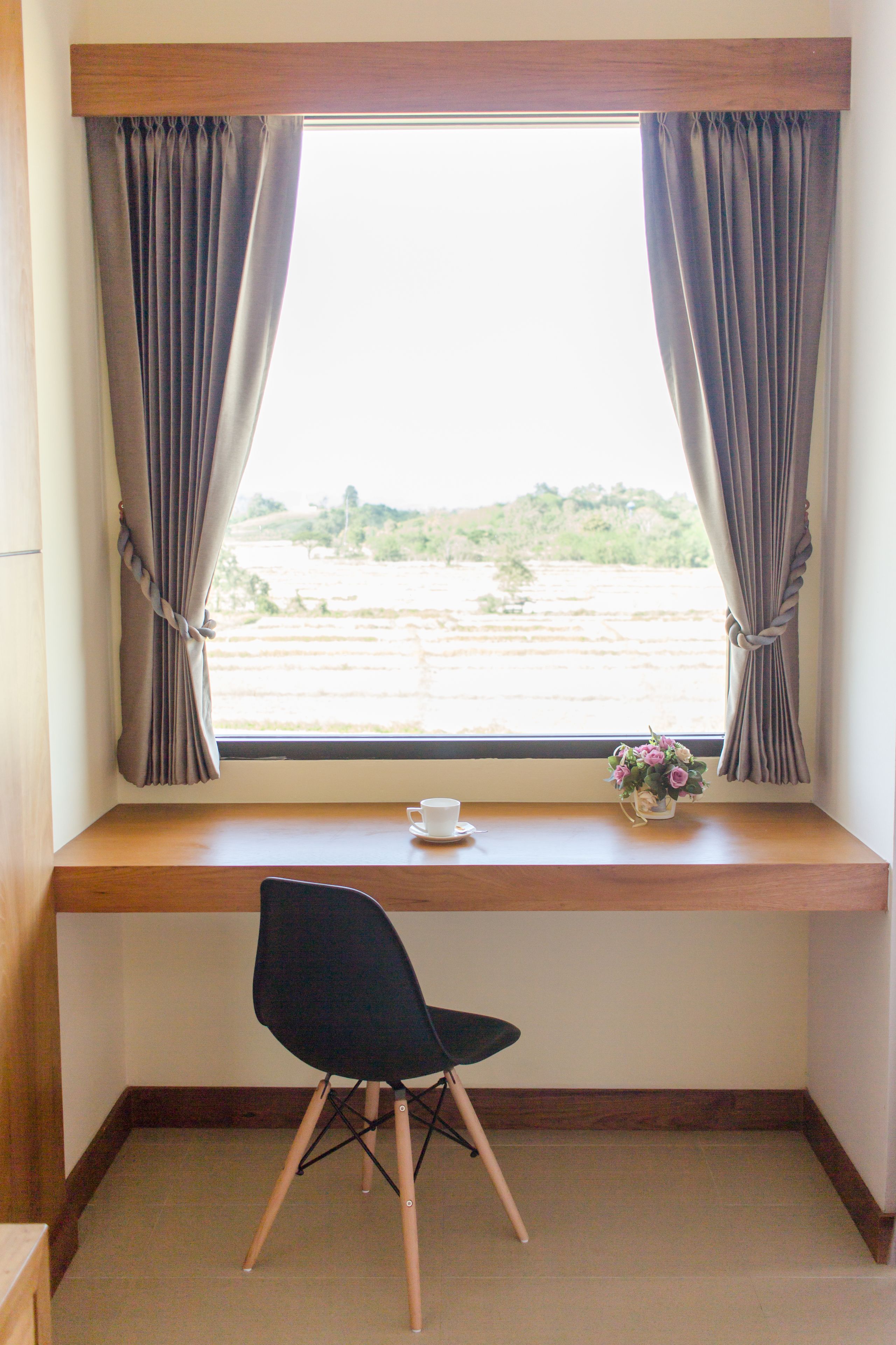 Una habitación con ventana, una silla y una mesita con una taza y flores.