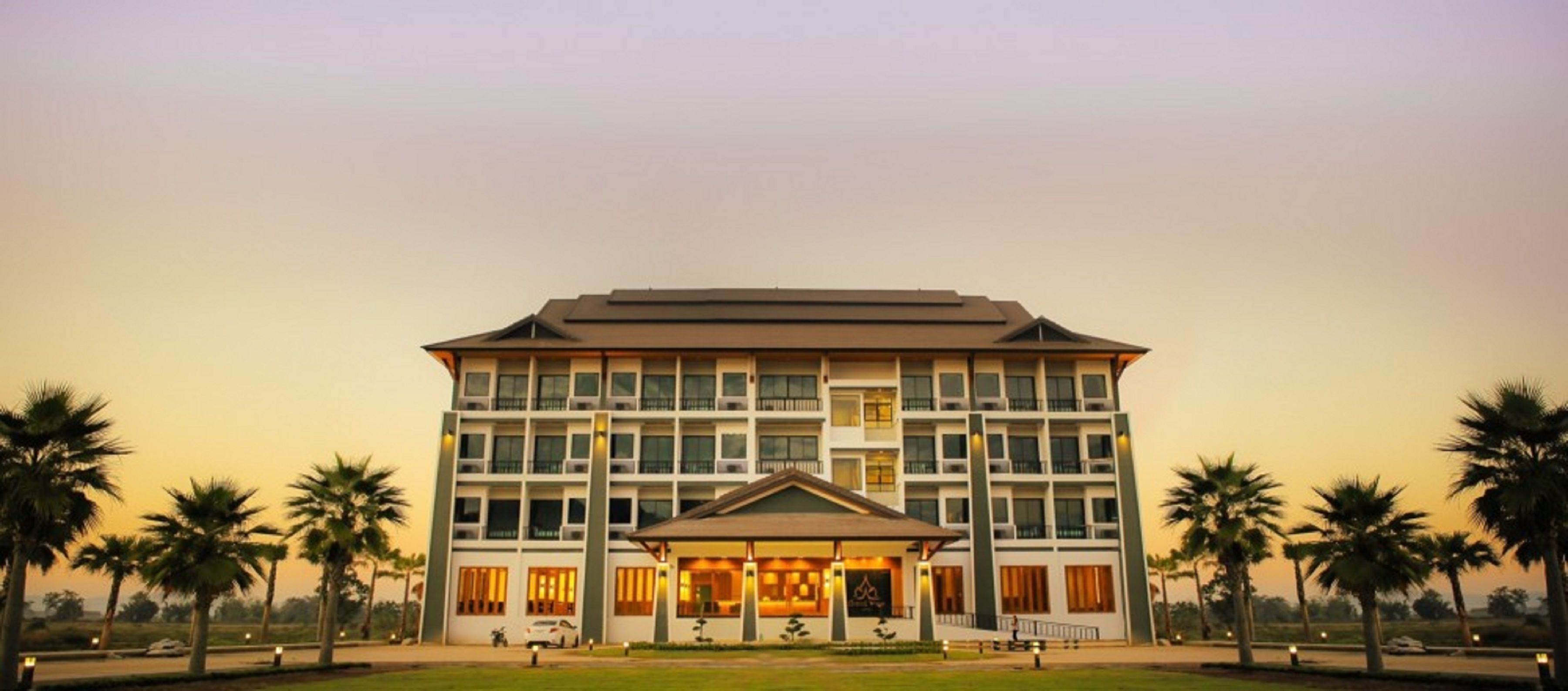 A multi-story hotel with a central entrance, surrounded by palm trees.