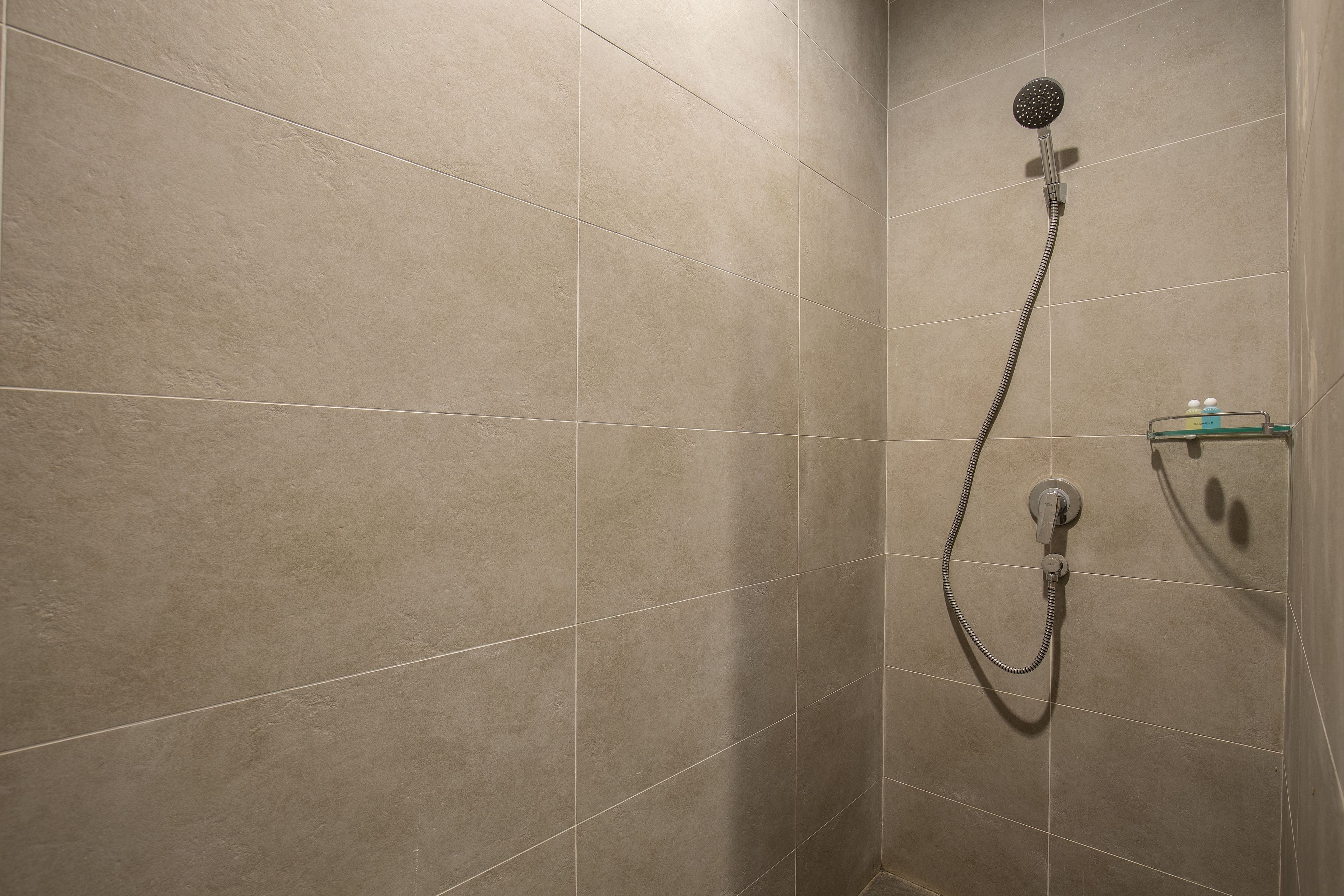A shower area with beige tiles and a handheld showerhead.