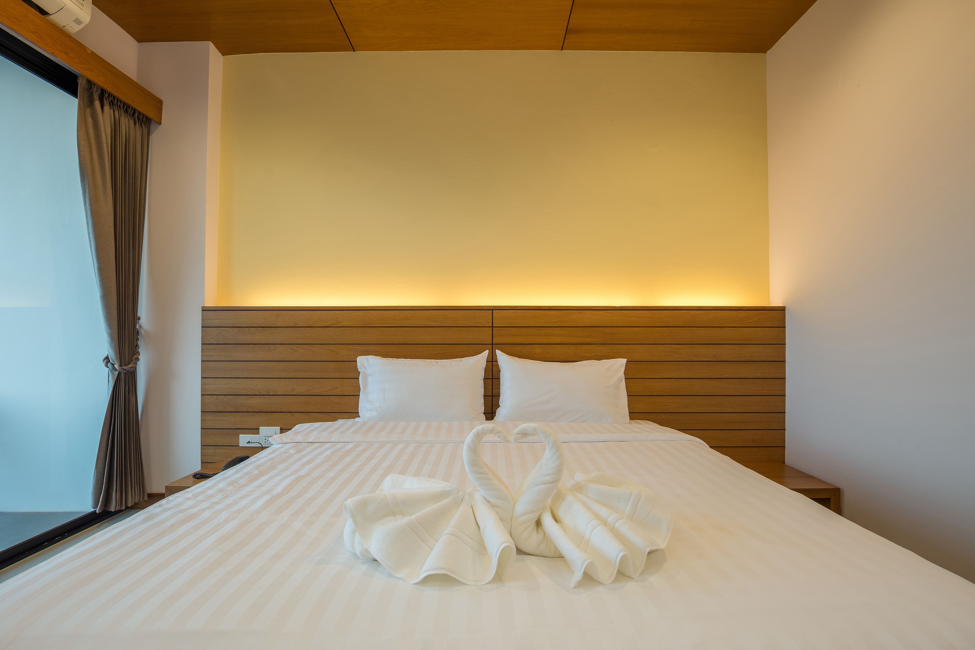 Une chambre d’hôtel avec un lit bien fait, une tête de lit en bois et une grande fenêtre avec des rideaux.