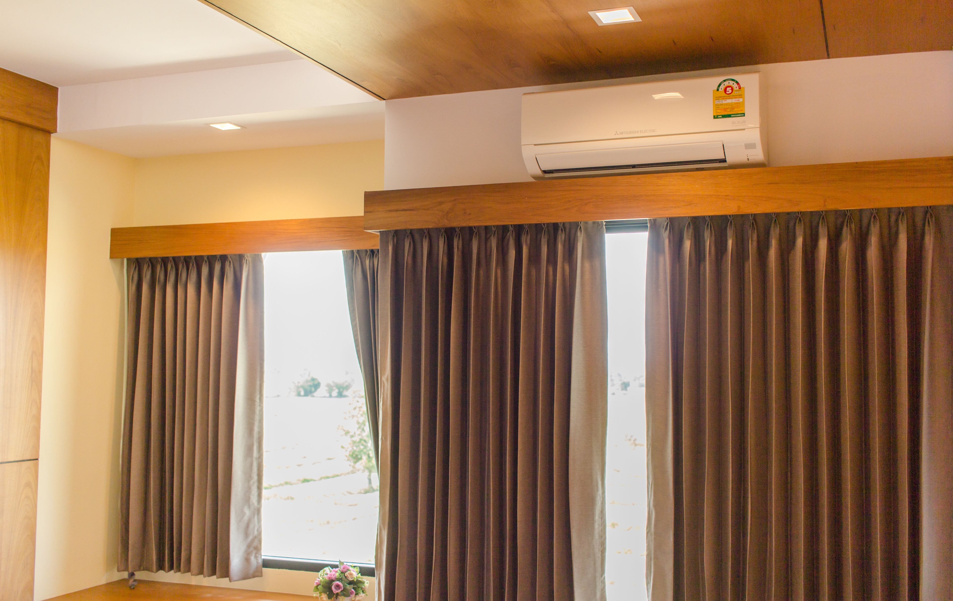 A hotel room with large windows, dark curtains, a ceiling-mounted air conditioner, and a wooden ceiling.