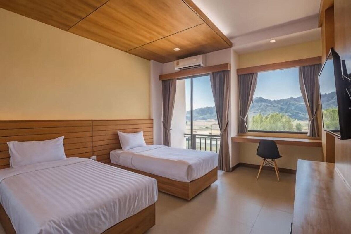 Hotelkamer met twee bedden, een bureau, een stoel, een televisie en een groot raam met uitzicht.
