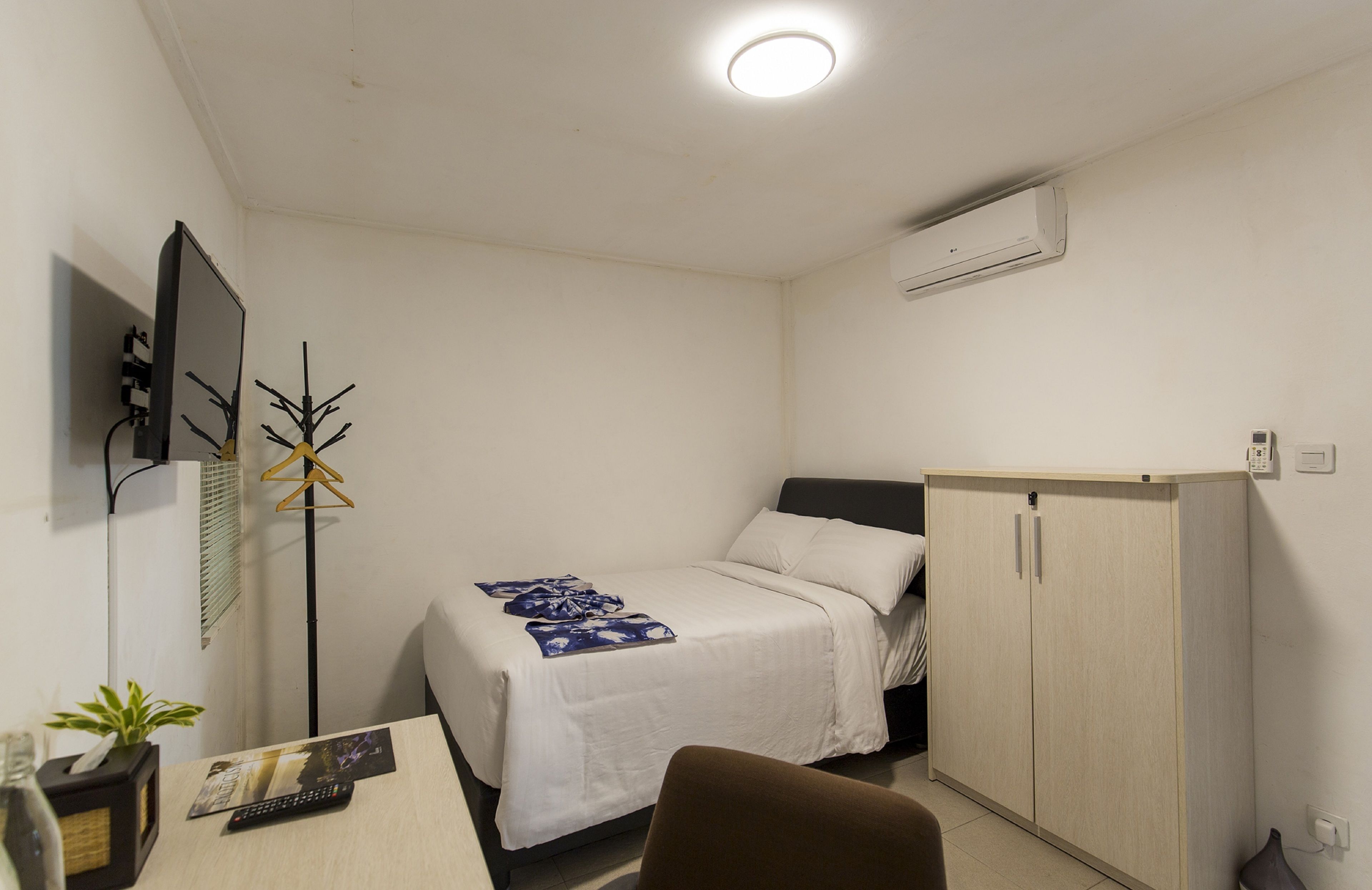 A small, neatly arranged bedroom with a single bed, a desk with a chair, a TV, and a wardrobe.