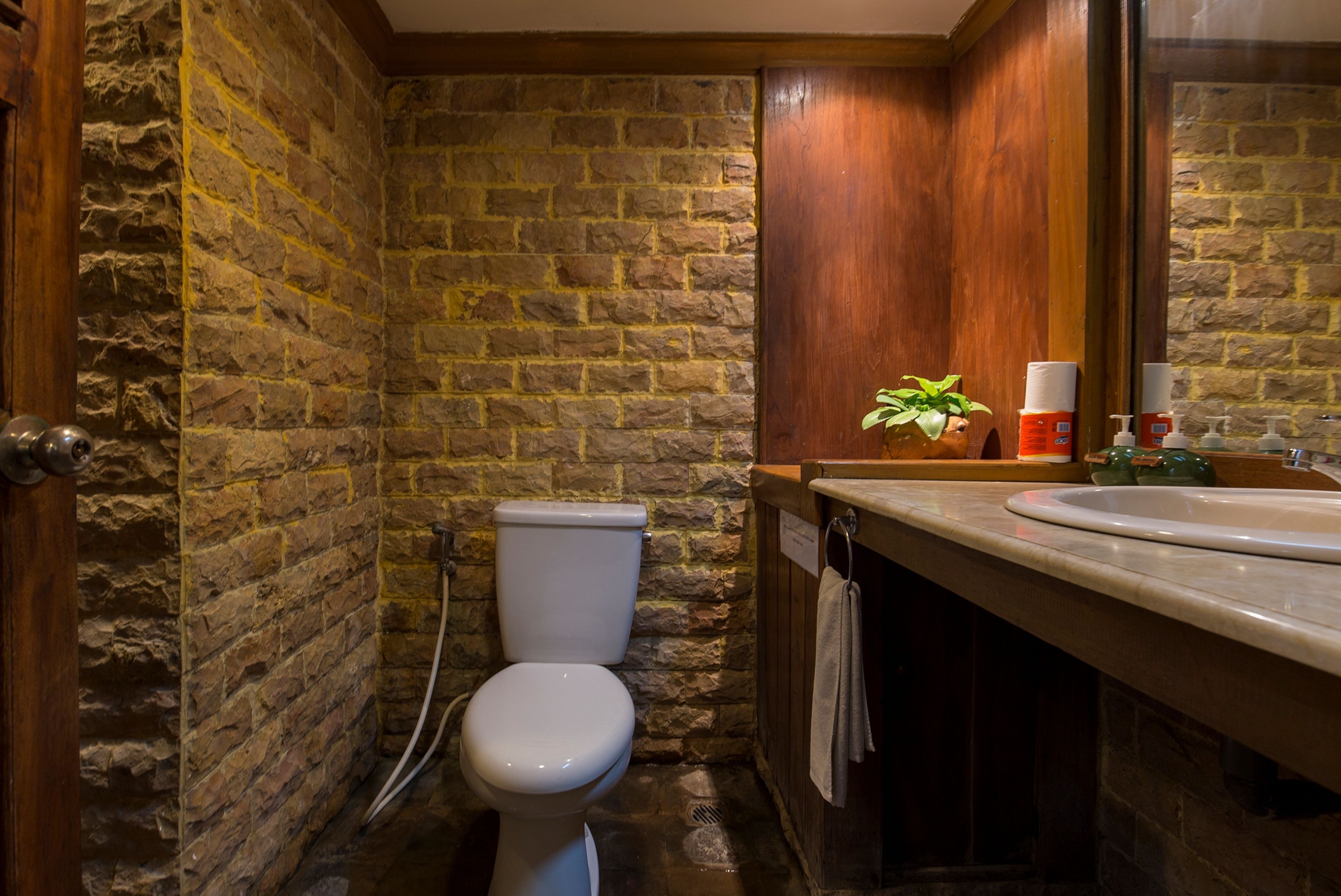 Un baño con pared de piedra, inodoro, lavabo y espejo.