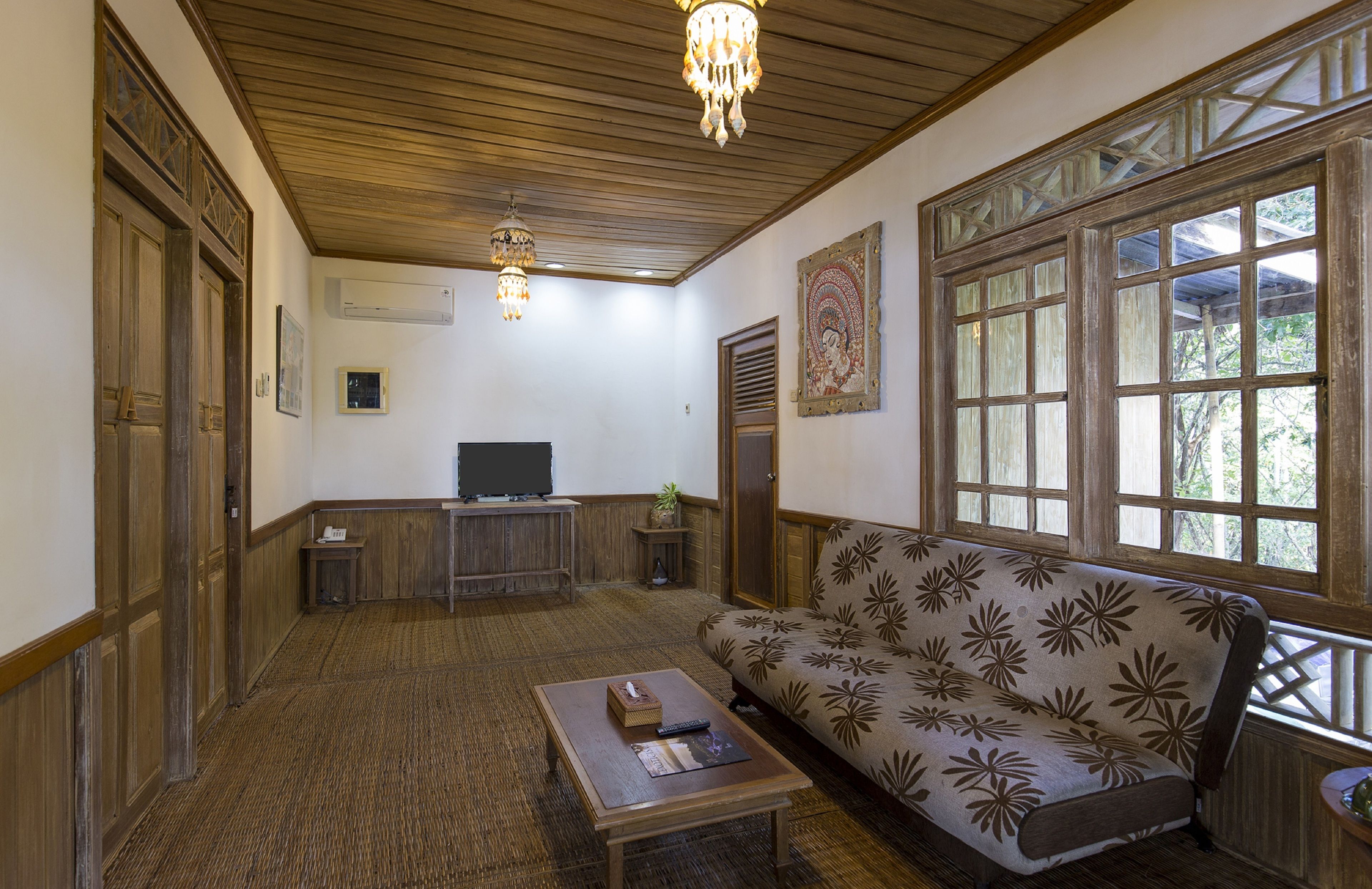A room with a wooden ceiling, a sofa with a floral pattern, a television, and a chandelier.