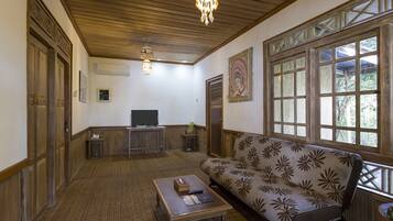 A room with a wooden ceiling, a sofa with a floral pattern, a television, and a chandelier.
