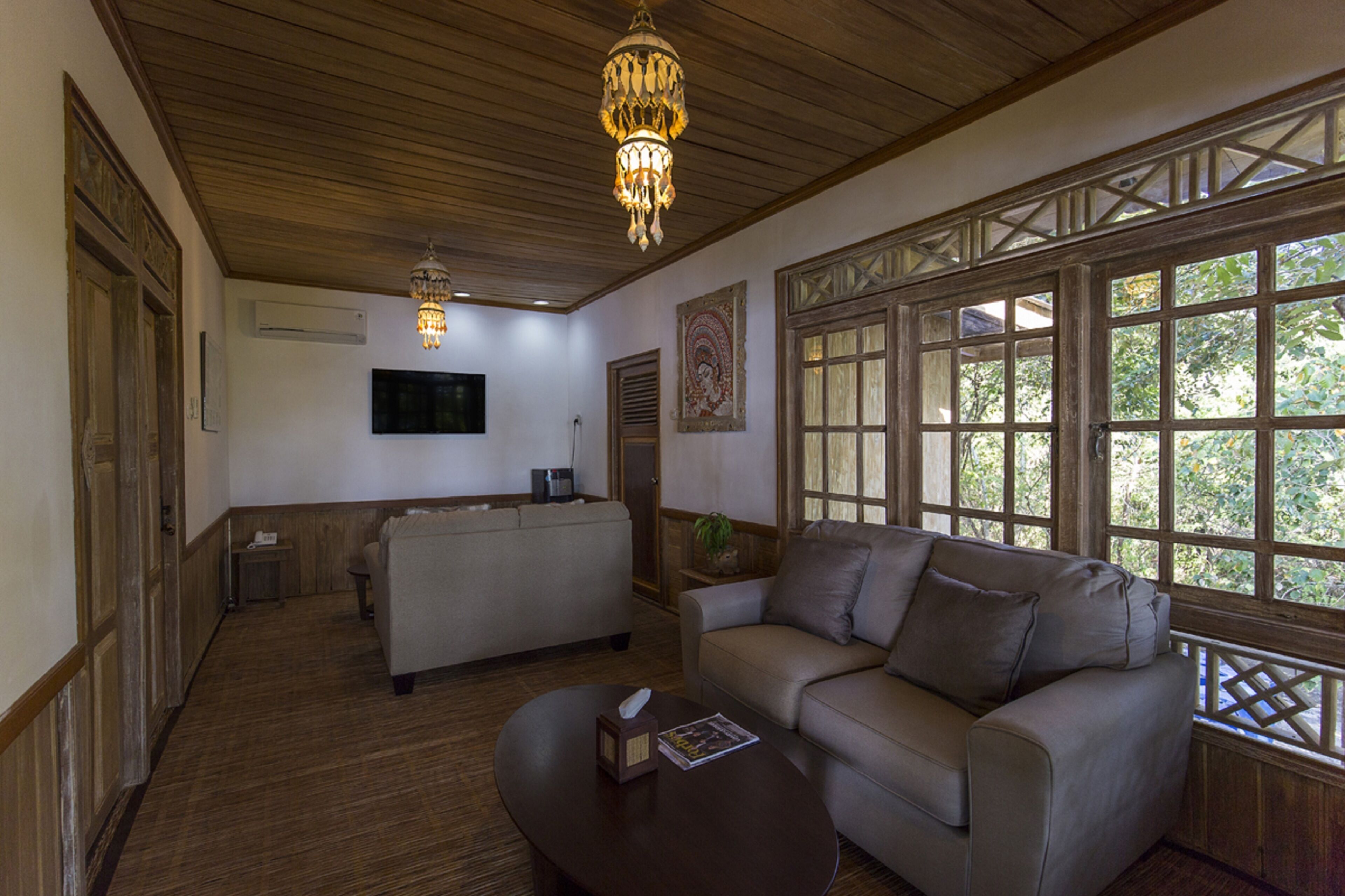A spacious living area with a wooden ceiling, a sofa, a coffee table, and a large window with a view of trees.