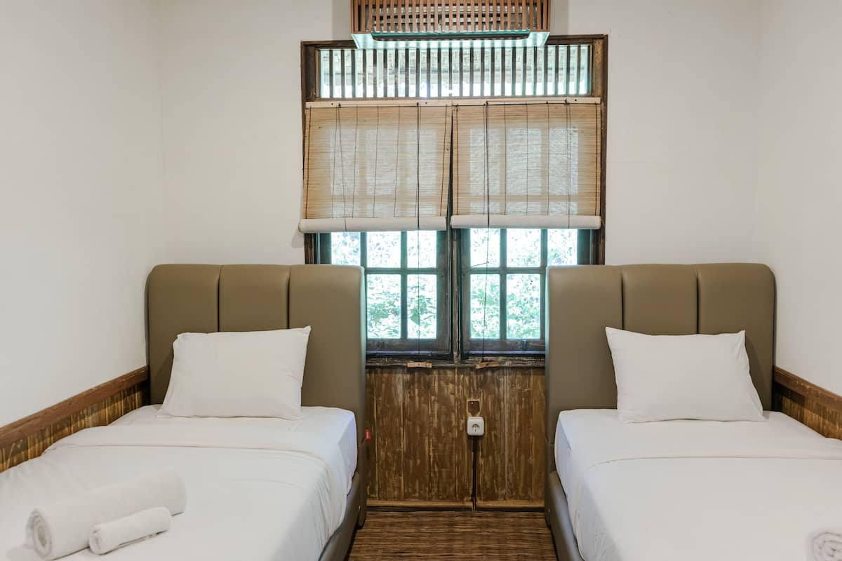 Habitación de hotel con dos camas, cabeceros de madera y una ventana con persianas de bambú.