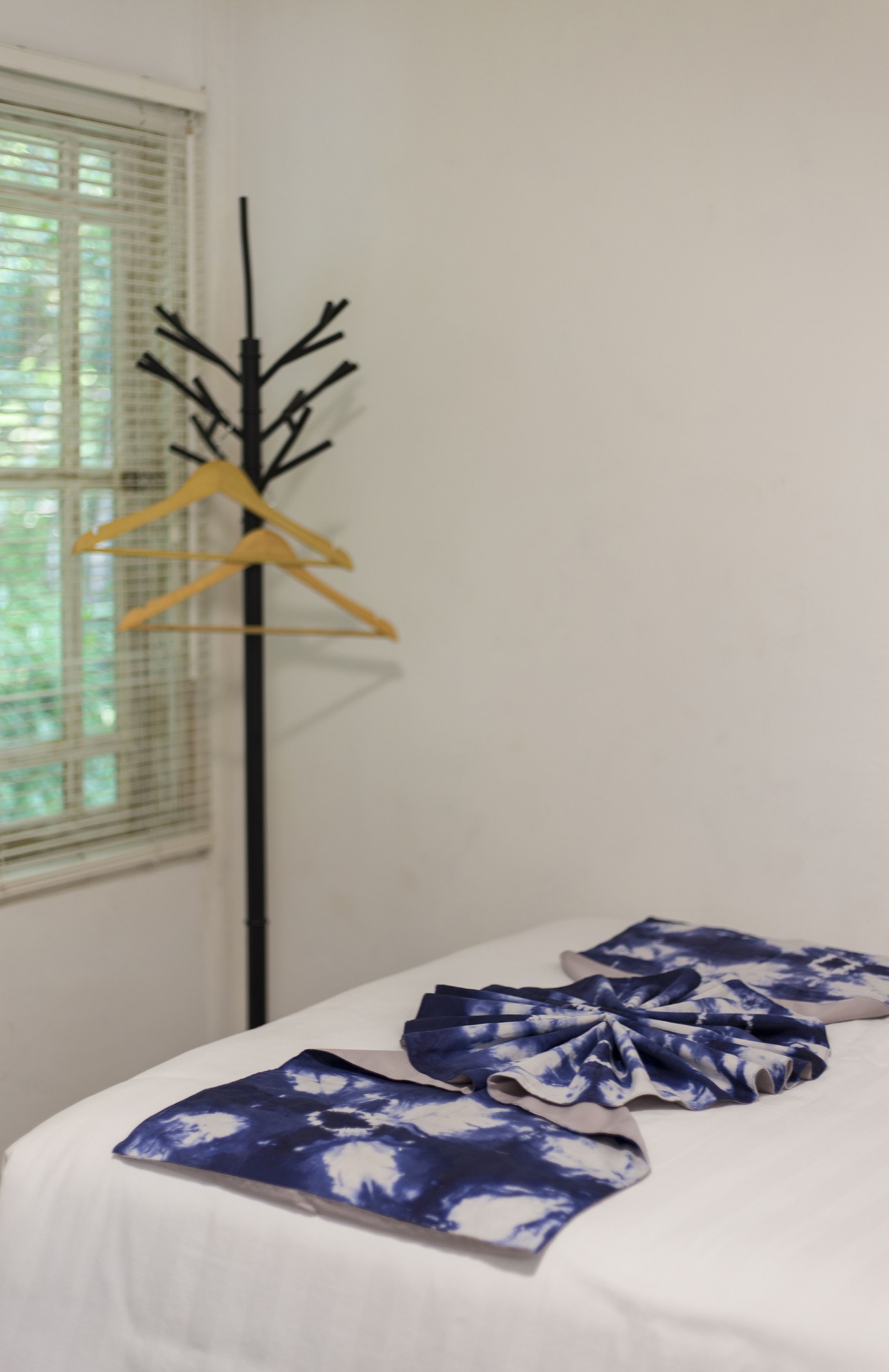Una habitación con una cama, una ventana con persianas y un perchero con perchas amarillas.
