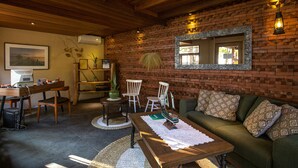 Una sala de estar acogedora con pared de ladrillo, vigas de madera en el techo, un sofá verde y una mesa de centro de madera.