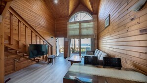 A wooden cabin interior with a TV, seating area, and a large window overlooking the beach. - Jeju Bada Walking Pension (Seogwipo)